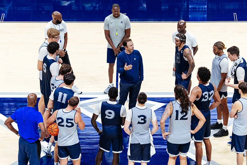 Coach Richard Pitino '05 leads a practice session at Xavier University surrounded by players in the gym.