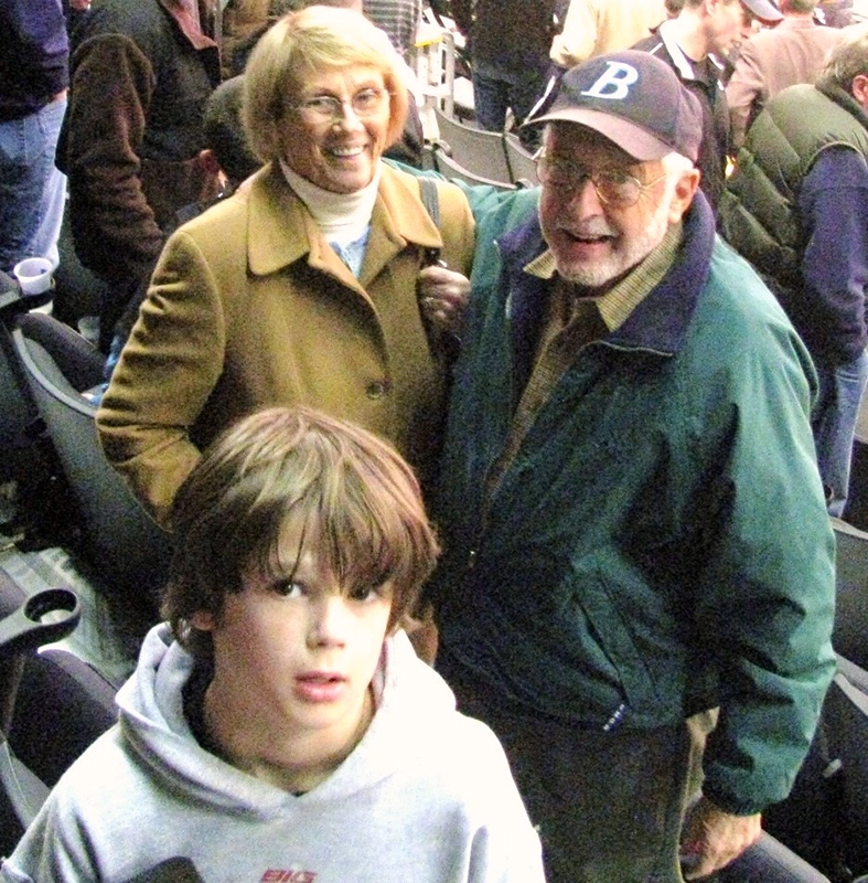 John Puleo, wearing a baseball cap, stands with his wife and grandson in the stands at a Friars basketball game.