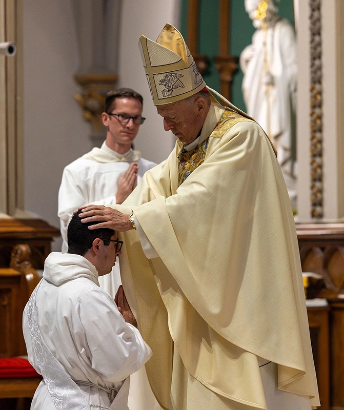 Cardinal of Catholic church rests is hands on the head of a kneeling priest during ordination.