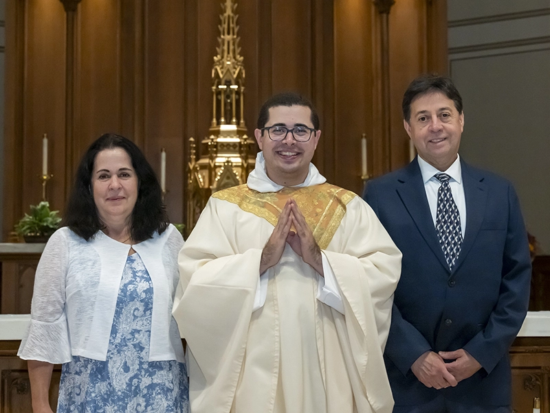 A newly ordained priest poses with his parents on a church altar.