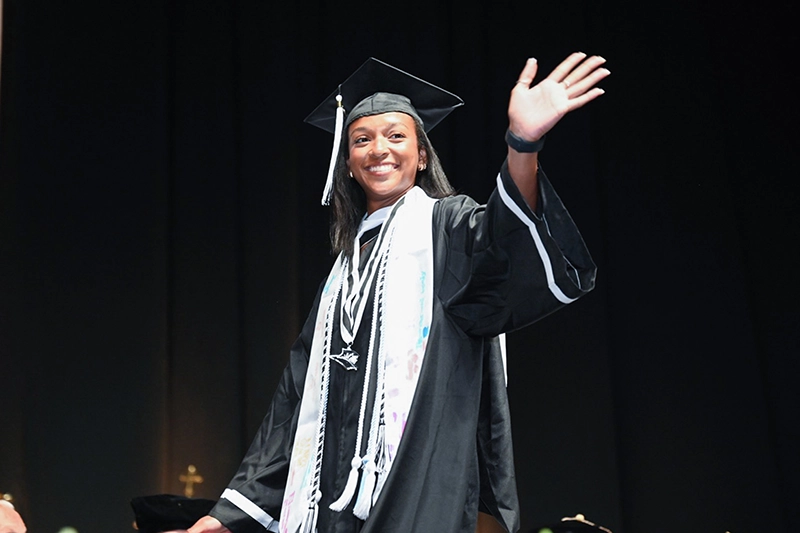 A student waves as she crosses the stage at the Class of 2025 commencement.