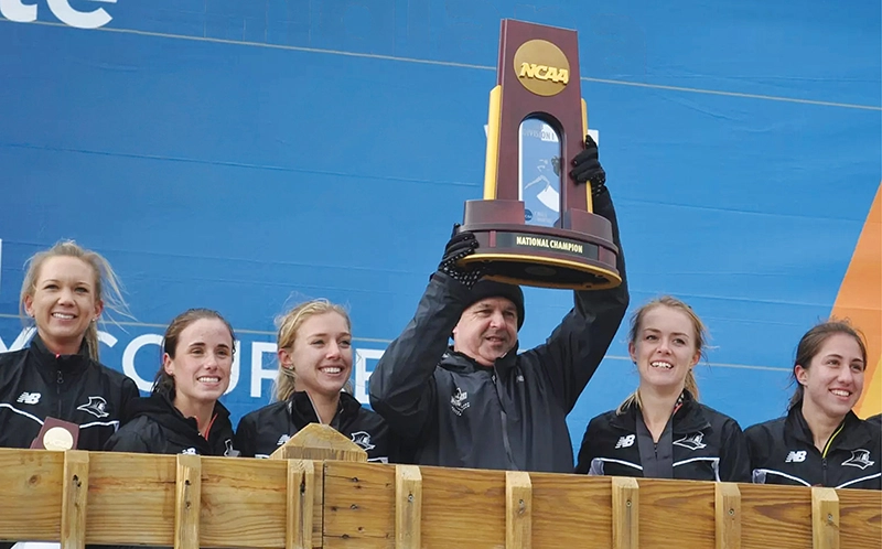 A man lifts a trophy in the air as five women smile