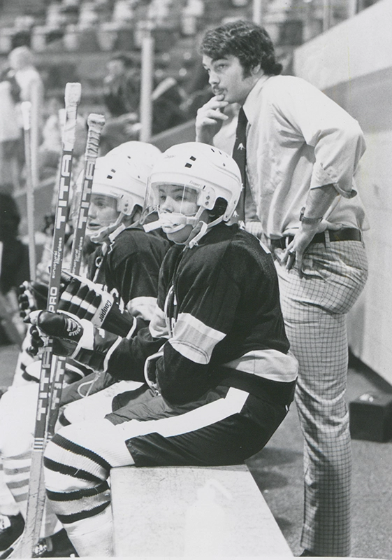 Coach Tom Palamara standing behind women's hockey players at a game.
