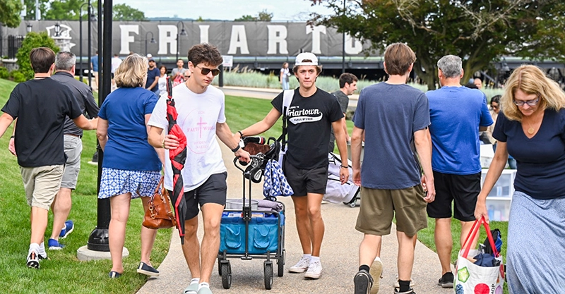 Families and new students in the Class of 2028 move belongings to campus with a Friartown sign in the background.