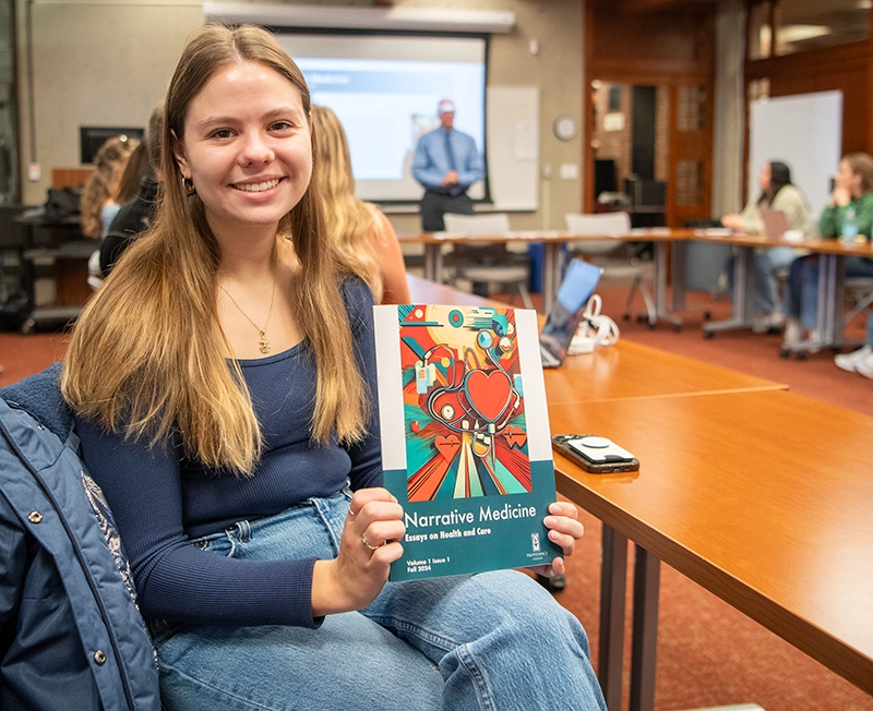 Rachel Medeiros '25 displays a print copy of the healthcare journal during a launch celebration held during Homecoming Weekend.