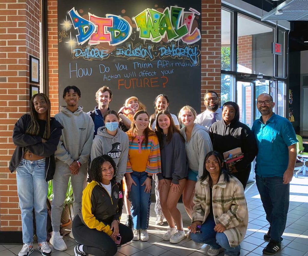 students and faculty in front of the Dialogue, Inclusion, and Democracy wall in Moore Hall