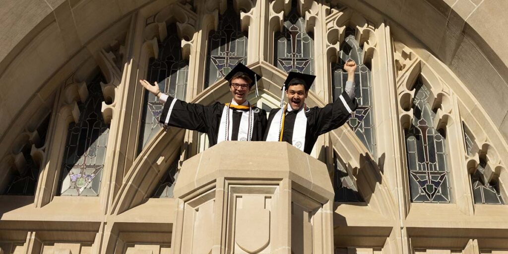 DiSpena and friend and Student Congress colleague Cole Patno celebrate in caps and gowns on the balcony in front of Harkins Hall